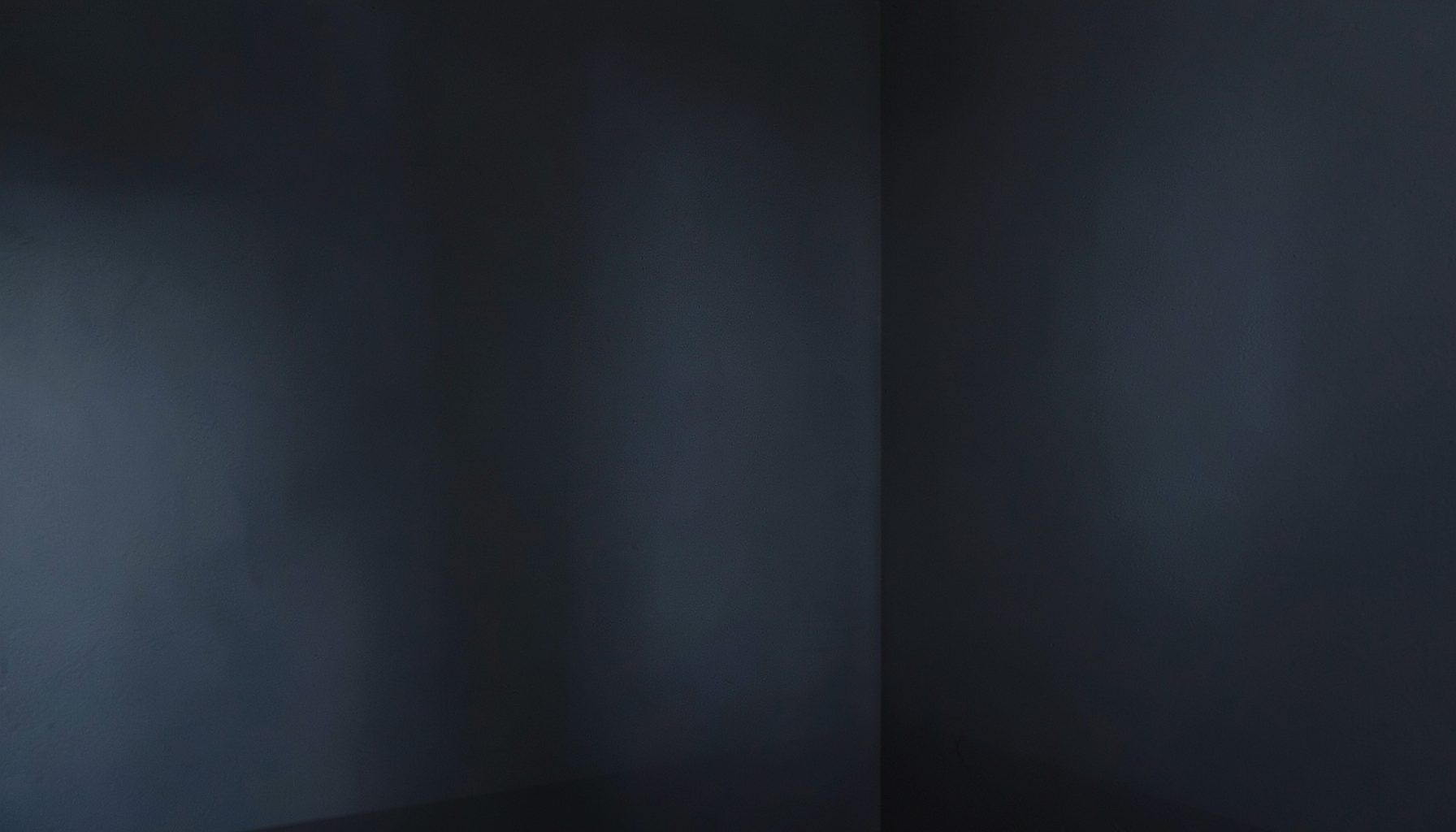 A dimly lit interior wall corner with subtle shadowing, cool gray and deep charcoal tones, conveying a quiet residential atmosphere.